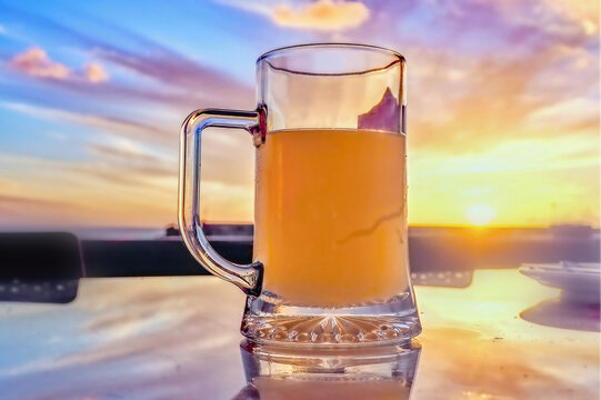 a filled beer pumpkin stands on a table, is photographed against the evening sky with setting sun in close-up. The beer looks golden and the tankard very big.
