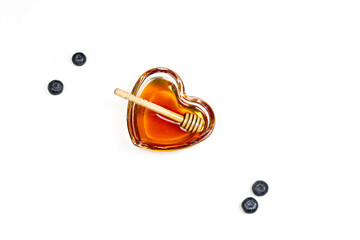 Heart shaped glass plate with honey and honey wooden dipper on white isolated background. Flat-lay image
