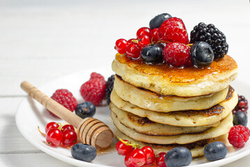Sweet Homemade Pancakes with berries, honey or maple syrup on white background. Morning breakfast concept.
