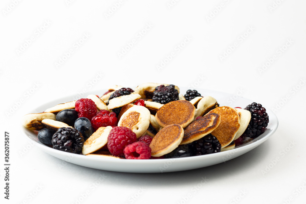 Wall mural trendy mini pancakes breakfast concept. tiny cereal pancakes with berries, honey or maple syrup on w