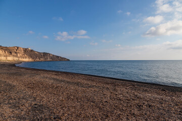 Kanakari beach on Santorini island in Greece. The background is a beautiful blue sky with white clouds.