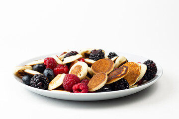 Trendy mini pancakes breakfast concept. Tiny  cereal Pancakes with berries, honey or maple syrup on white background. Kids lovely breakfast concept.