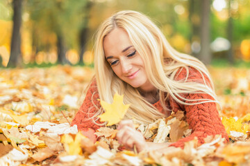 Beautiful young blond hair caucasian woman lies down on leaves at the autumn park