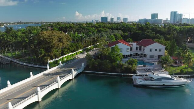 Expensive home with yacht at the private pier, USA. 4K aerial close view on Star Island with Miami downtown on a background. Lavish nature of a green tropical island. Stock video for travel business.