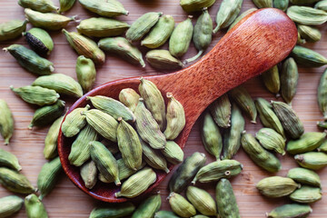 Dry cardamom pods in a wooden spoon.