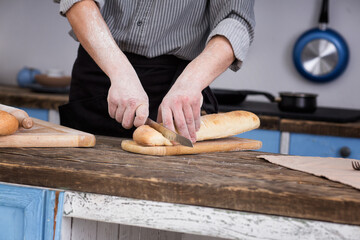 Striped baguette on a board. The knife is in men's hands. Kitchen view
