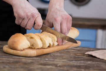 Striped baguette on a board. The knife is in men's hands. Kitchen view
