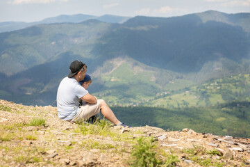 Naklejka premium Father shows little son the view from the top of the mountain. The boy listens carefully to dad. Father and son relationship concept