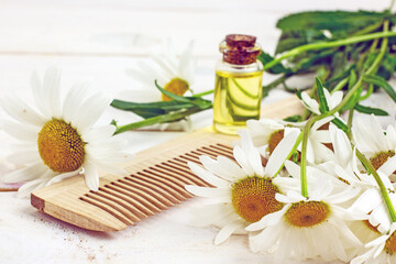 Chamomile essential oil in a transparent bottle next to chamomile flowers, body brush and wooden comb