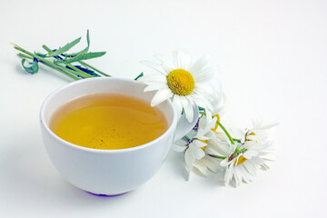 Chamomile tea. Flower tea in a white mug on a white table, near daisy flowers,copy space