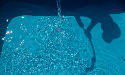 Der Schatten von einem Kind mit Gartenschlauch beim Füllen des Swimmingpools