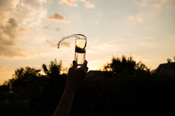 Splash of water in a glass. Flying water. A glass of water in a man's hand in the sunset.