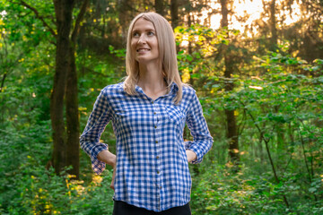 Portrait of a beautiful smiling European blonde girl in a shirt in the forest at sunset, copy space.