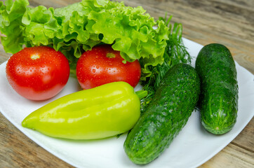Fresh juicy vegetables peppers, tomatoes, cucumbers lettuce leaves with water drops beautifully laid out on a white plate close-up. Vegetables are in the form of a funny face