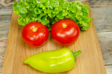 Fresh juicy vegetables peppers, tomatoes, cucumbers lettuce leaves with water drops are beautifully laid out on a wooden Board close-up. Vegetables are in the form of a funny face, top view