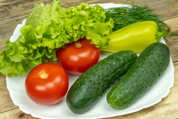 beautiful fresh, juicy vegetables on a white plate: fresh peppers, tomatoes, cucumbers, lettuce, dill