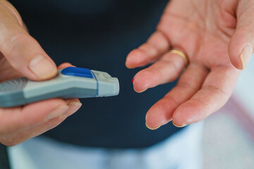 Medicine, Diabetes, Glycemia, Health care and people concept - close up of female using lancelet on finger to checking blood sugar level by Glucose meter