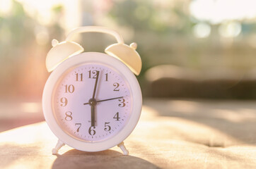 white alarm clock stands on the sofa in the sunlight. Beautiful background with alarm clock