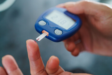 Medicine, Diabetes, Glycemia, Health care and people concept - close up of female using lancelet on finger to checking blood sugar level by Glucose meter