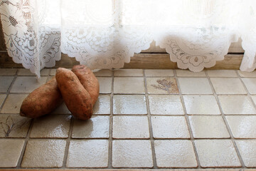 Sweet potato on the light tiles near the window and curtain, retro kitchen