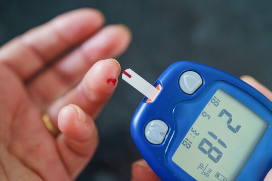 Medicine, Diabetes, Glycemia, Health care and people concept - close up of female using lancelet on finger to checking blood sugar level by Glucose meter