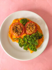 Vegan dish with baked tomatoes and brocolli on pink background 