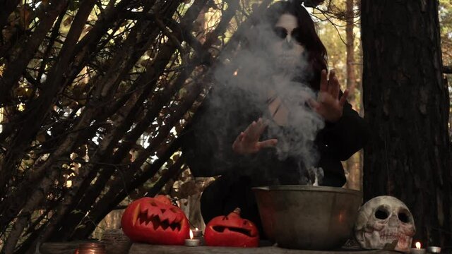 Witch brews a potion in a cauldron from which the smoke billows slow motion. Theme of the occult and esoteric rituals in the wild nature. Mystical wizard uses a cauldron to perform a magic ceremony.