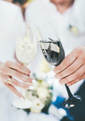 Close-up of a glass in a black and white rim in the hands of the bride and groom on a wedding day. The ring on the girl finger. Drink champagne together