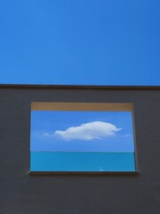 View of single cloud in blue sky through a window frame on gray wall of modern building