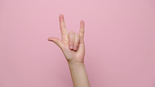Rock-n-roll concept. Close up female hand waving with horns gesture, isolated on pink studio background with copy space for advertisement. With place for text or image. Body language