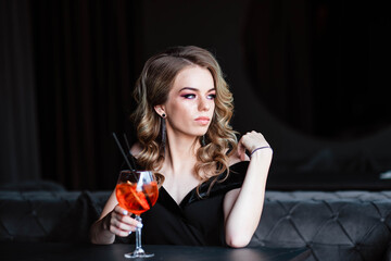 Beautiful blonde, young girl holding an aperol spritz. Aperol cocktail syringe in a glass. Portrait...