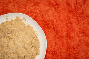 maca root powder on white ceramic plate against red textured paper, superfood concept