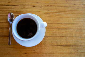 Black coffee in white cup on wooden table. Coffee drinking concept. Coffee cup and spoon top view photo.
