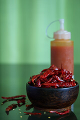 Dried chilli in wooden bowl and red hot chilli sauce bottle.