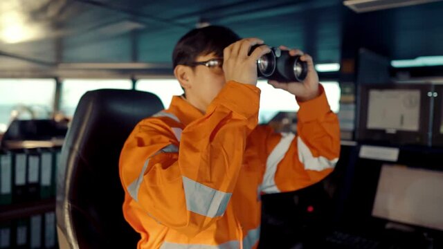 Filipino deck Officer on bridge of vessel or ship wearing coverall. He is looking through binoculars. COLREG navigaton watch at sea