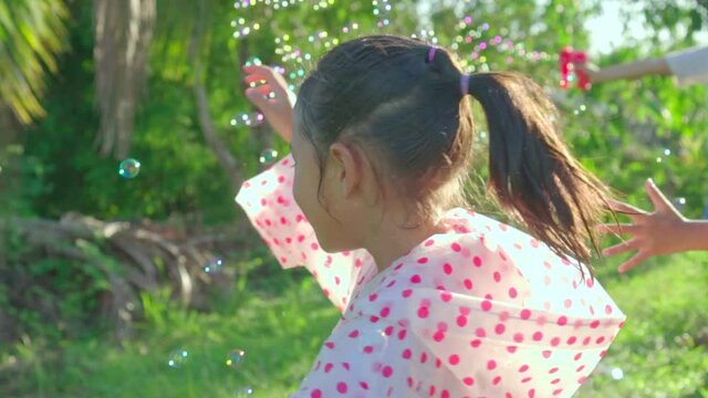 Asian little girls in rainwear is playing air bubble from spray gun with her mom at the backyard. Activities that indicate of love freedom and joyful in babyhood. Slow motion. Record in 120 fps.