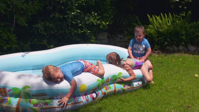 Little kids run, play and splash in a backyard inflatable pool