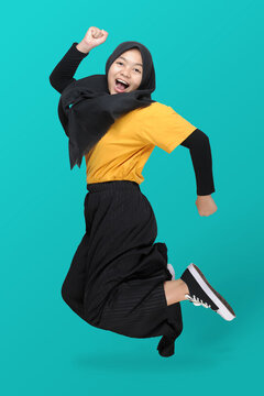Full Length Body Size View Of Cute Asian Teenager Girl Wearing Headscarf Jumping Clench Hands With A Smile On Her Face. The Concept Of Happiness, Carefree And Positive