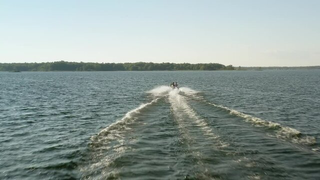 Drone following a pleasure craft as it speeds on shimmering water into the sun