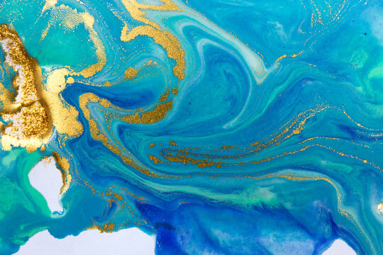 Gold and blue mixed inks splattered on white paper background.