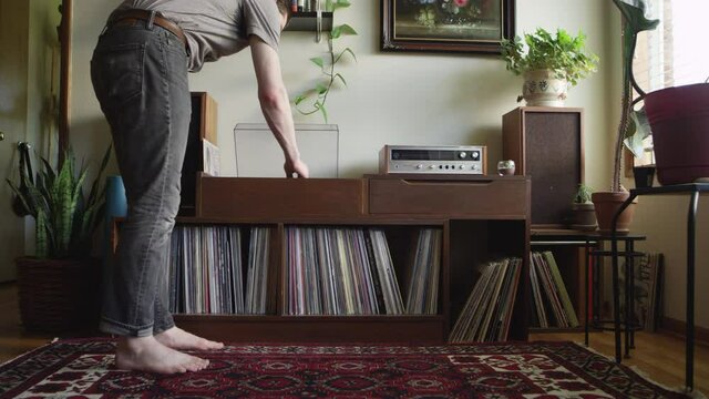 Barefooted hipster man walks up to a vintage stereo and flips a vinyl record