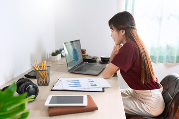 Asian woman working with laptop and document in living room remotely or work from home concept