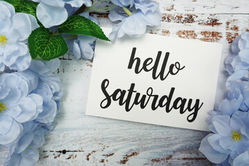 Hello Saturday Card with Blooming flower on wooden background