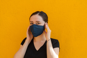 Woman wearing a blue facemask, side shoot, outdoors with bright yellow background