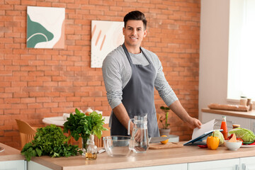 Young man with recipe book preparing fresh lemonade in kitchen