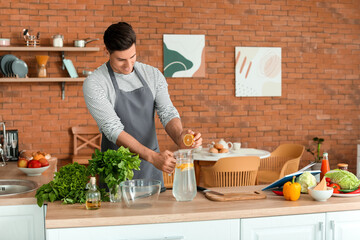 Young man with recipe book preparing fresh lemonade in kitchen