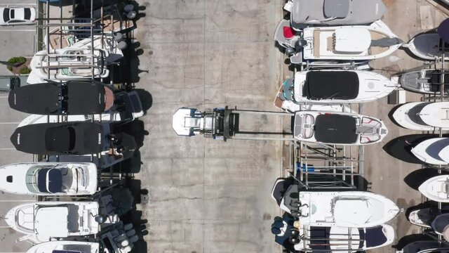 Top-down view on forklift approaching to the parked yacht at the multi-level yacht parking. Beautiful slow motion drone video for yacht business. 4K aerial video of water transportation, Miami