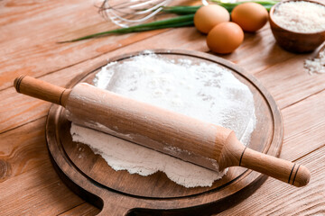 Board with rolling pin and flour on wooden table