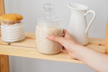 Woman taking jar with rice from shelf in kitchen