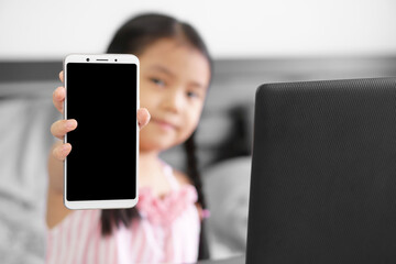 Asian child or kid girl smile hold smartphone or mobile phone for show present empty black screen display to play or study online and work at home on computer